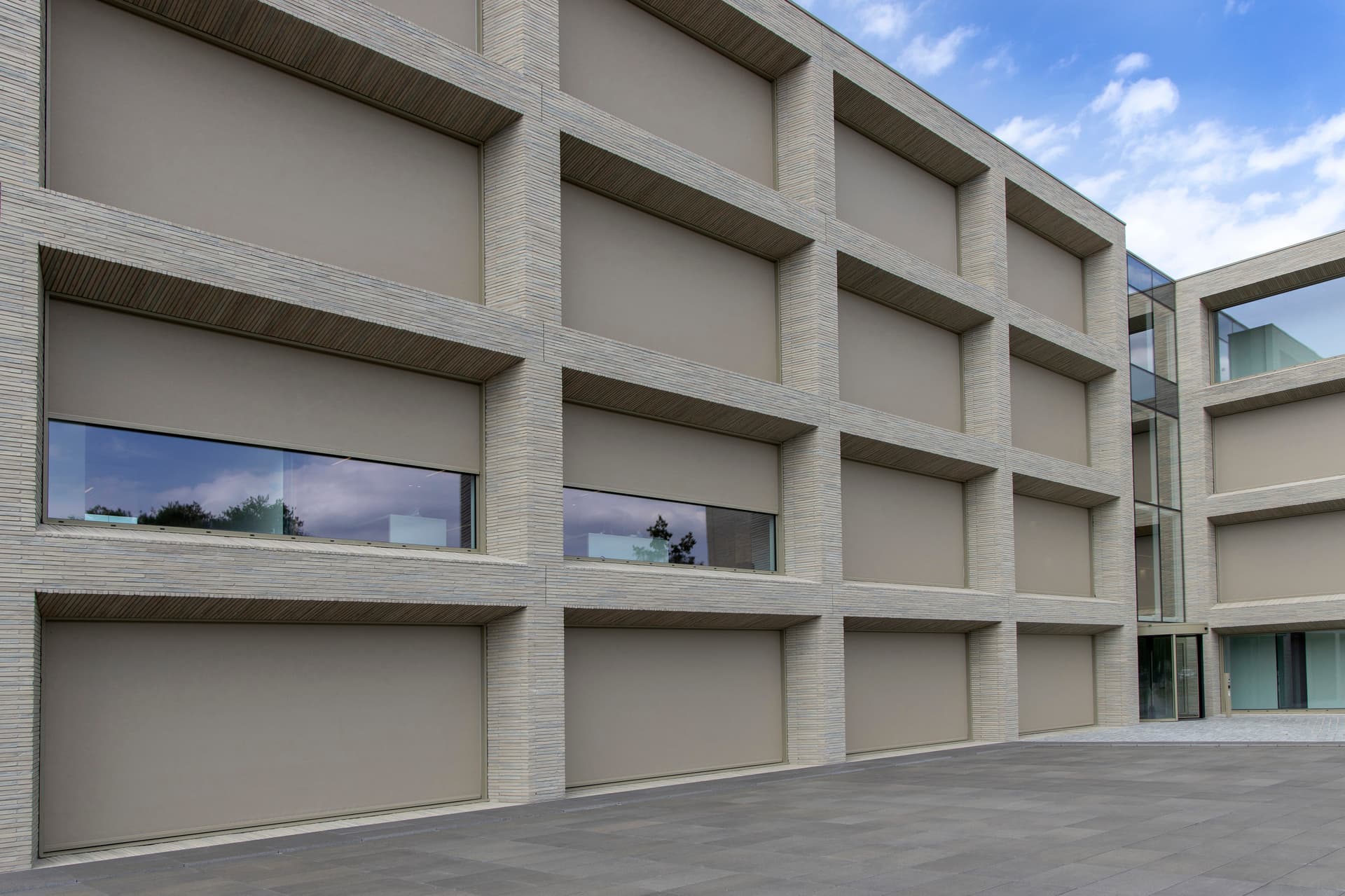 Wind‑resistant Brustor outdoor ZIP screens fully covering the windows of a modern office building for optimal sun protection and privacy