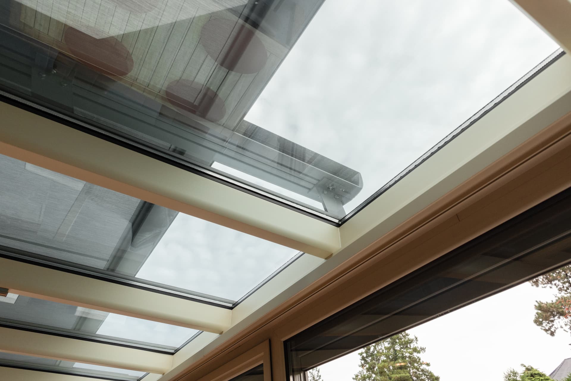 Brustor B129 under‑glass awning installed beneath a glass roof, providing discreet sun protection with taut fabric and slim guides